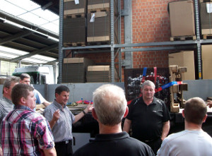 Paul Kummer mit mehreren Mitarbeitern vor einem offenen Plateau-Auflieger, welcher mit einer Gitterbox beladen ist, die durch Spanngurte und Paletten gesichert wurde, bei der Unterweisung zur Ladungssicherung